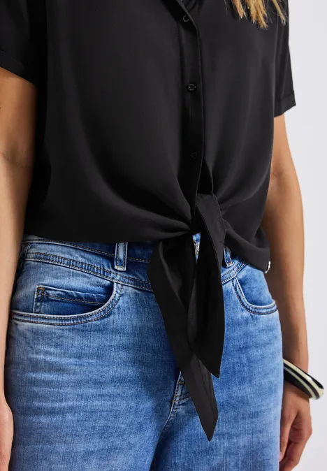 Frau trägt schwarze Bluse mit Knoten und blaue Jeans.